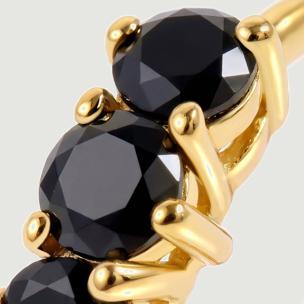 Faceted black stones sit in polished yellow gold plated prongs in this close view.