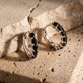 White rhodium plated black stone hoops lean against layered travertine blocks.