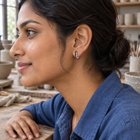 A woman with dark hair in a bun wears a white rhodium plated black onyx hoop beside a wooden workbench.