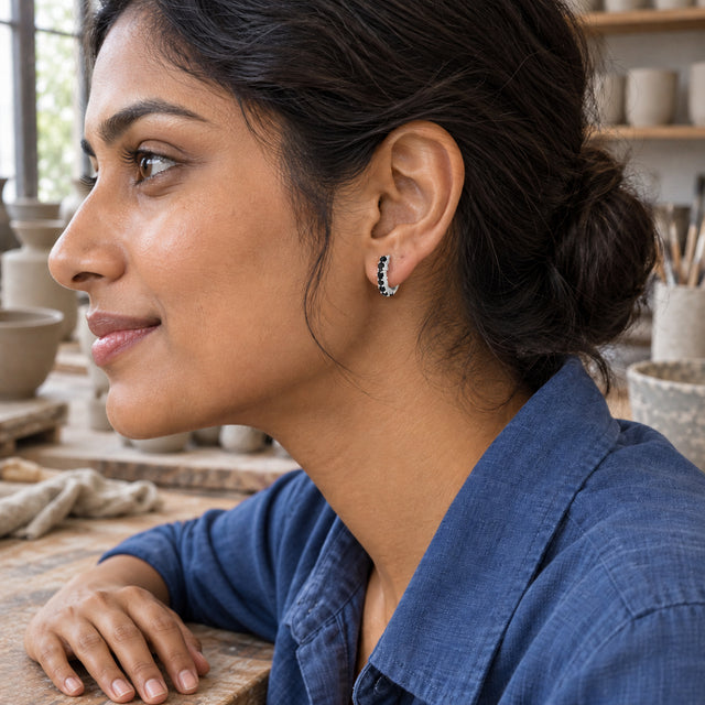 A woman with dark hair in a bun wears a white rhodium plated black onyx hoop beside a wooden workbench.