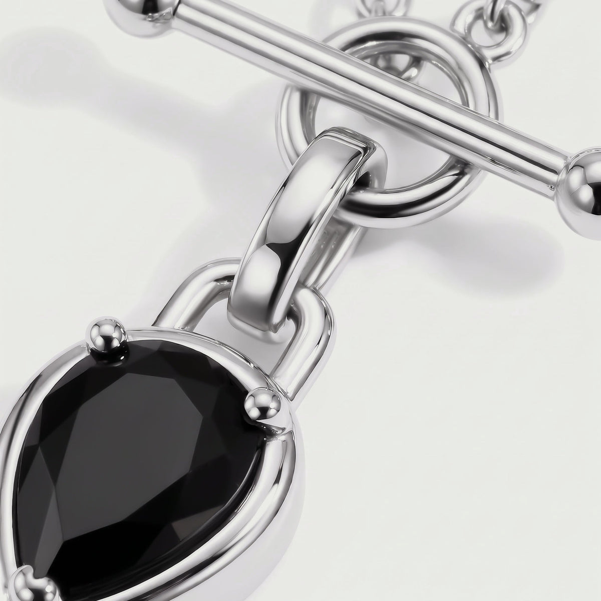 The black gemstone facets sit inside a reflective silver-tone setting beside a curved connector and circular clasp.