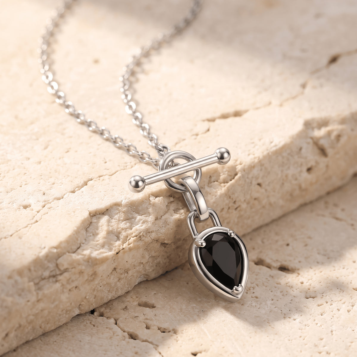 A silver-tone chain drapes over pale stone with its bar clasp and black pendant hanging toward the lower edge.