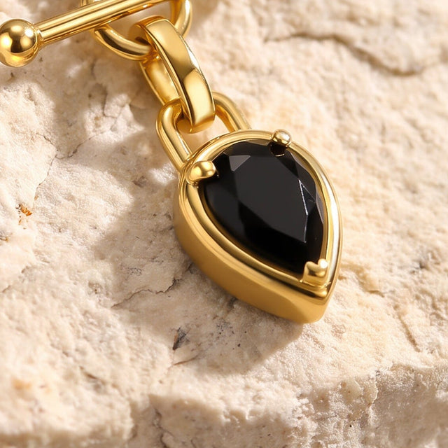 An angled close view of a black pear-shaped pendant reveals the depth of its gold-tone setting against pale textured stone.