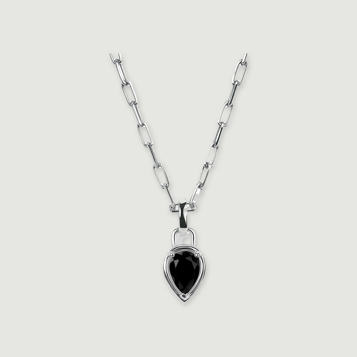 A silver-tone chain and pear-shaped black pendant are centered on a softly shadowed gray surface.