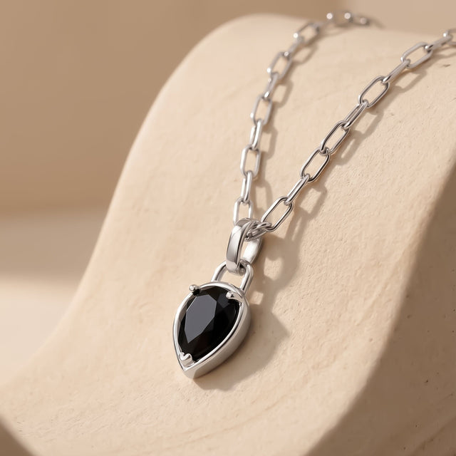 A rhodium plated necklace rests on pale stone with its black pendant pointing downward.