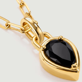 A close view shows black stone facets, three gold-tone prongs, and a polished pendant bail.