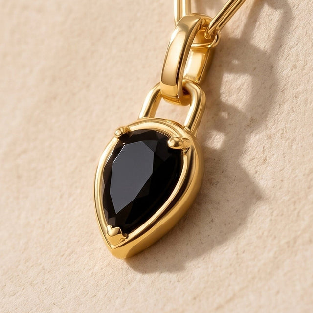 An angled close-up reveals the raised gold-tone setting around a pear-shaped black stone.