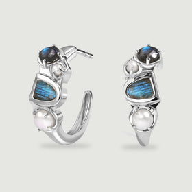 A pair of polished white rhodium hoops displays blue flashing labradorite and white pearls against a light gray background.