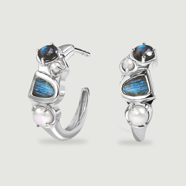 A pair of polished white rhodium hoops displays blue flashing labradorite and white pearls against a light gray background.