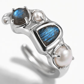 A close view shows the raw blue labradorite center, round upper stone and two pearls in a polished white rhodium hoop.
