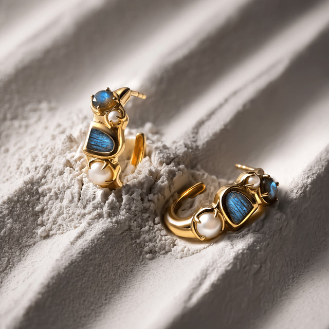 Yellow gold plated labradorite and pearl hoops lie together across ridges in a clean light colored surface.
