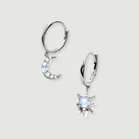 A pair of silver hoops with a crescent moon and a starburst charm rests on a light gray surface.