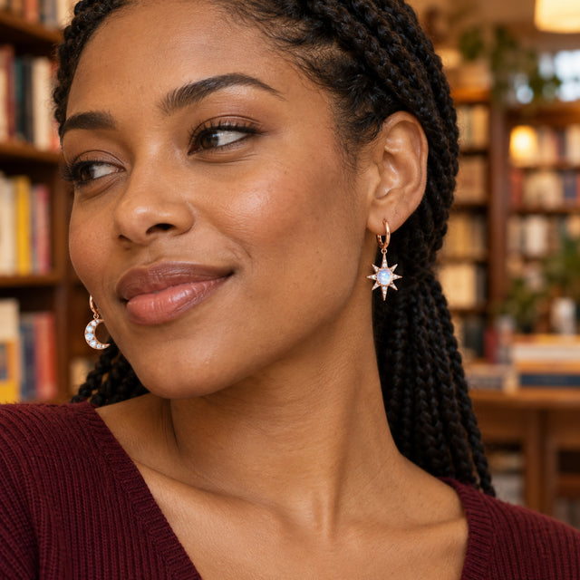 A woman with braided hair wears rose gold moonstone hoop earrings beside blurred bookshelves.