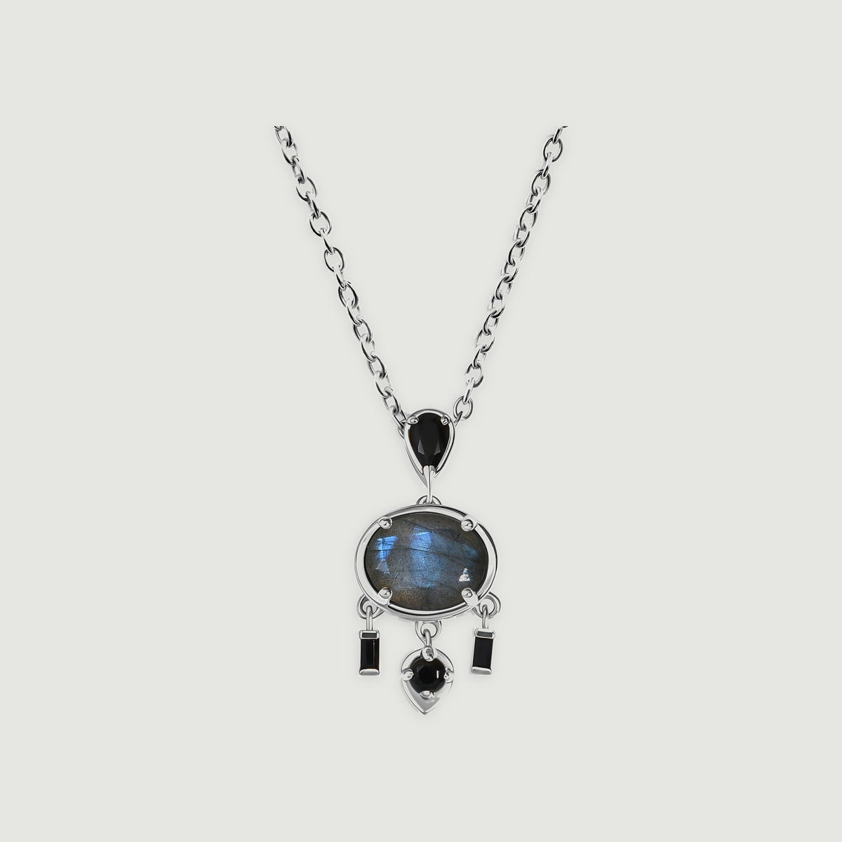 A white rhodium plated necklace with an oval blue grey labradorite and black stone drops rests on a light grey background.