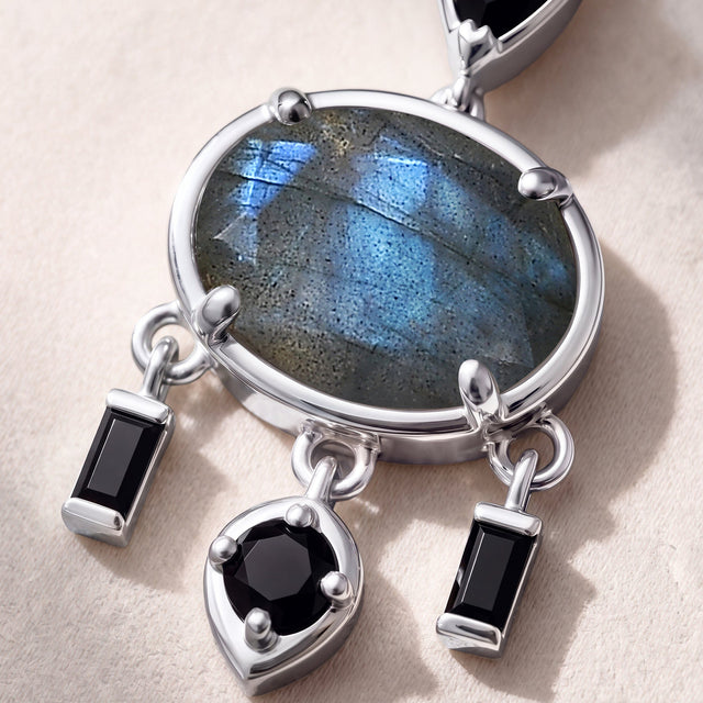 A close view shows blue reflections in an oval labradorite surrounded by polished white metal and dangling black stones.
