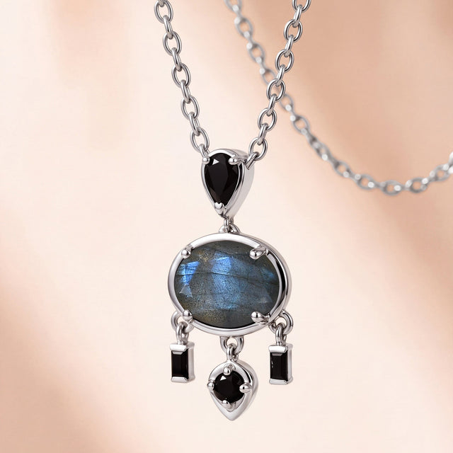 An angled white rhodium plated pendant lies on a pale stone surface with its chain links and raised settings visible.