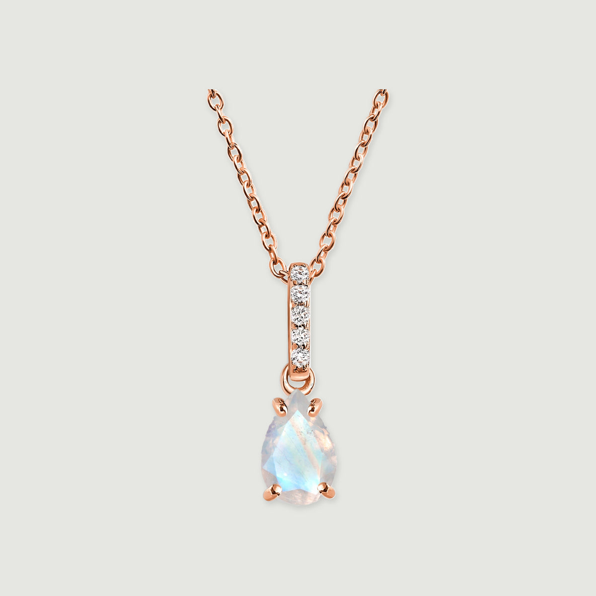A rose gold chain and four rounded prongs frame an iridescent pear-shaped moonstone on a soft gray surface.