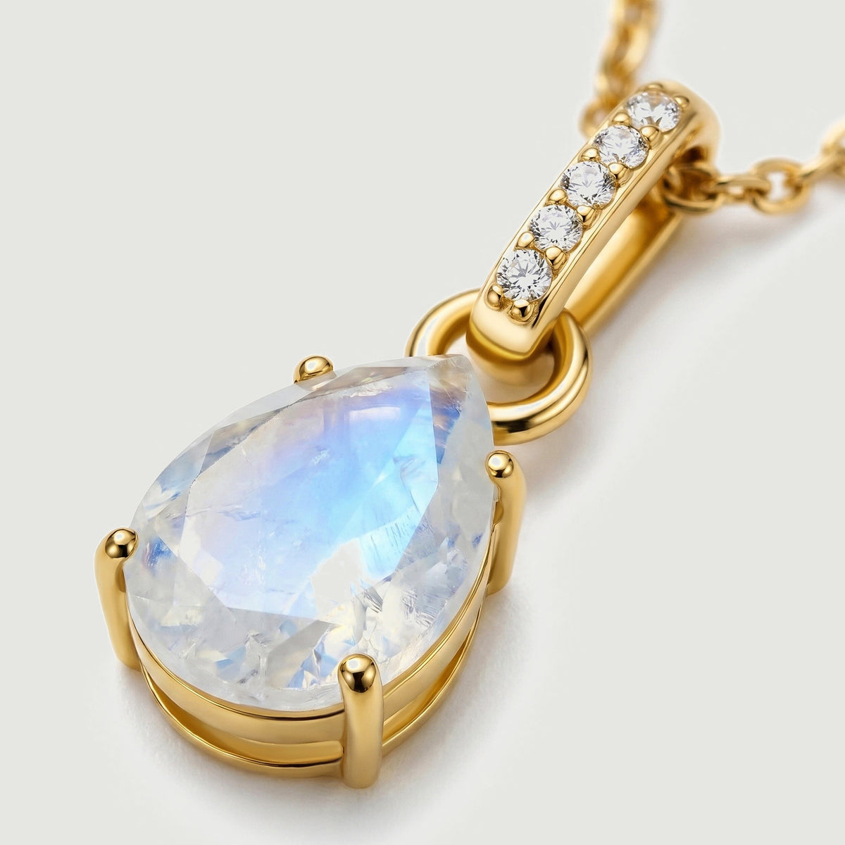A close angled view shows five clear stones along the yellow gold bail and the moonstone held in rounded prongs.