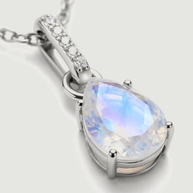Blue and lavender reflections cross the faceted moonstone beside polished silver prongs and a stone-set bail.