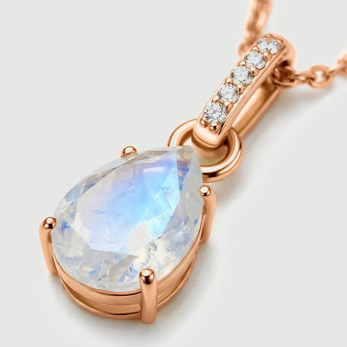 An angled macro view reveals the rose gold setting, pear-shaped moonstone facets, and five clear stones above the pendant.