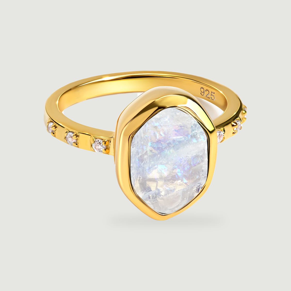 A yellow gold ring with an irregular pale moonstone and small clear stones rests on a light grey surface.
