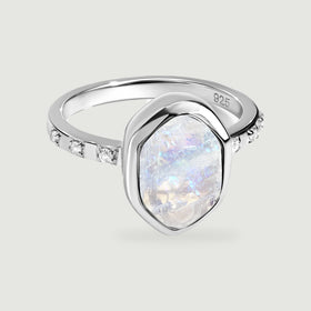 A silver ring shows a raw iridescent moonstone, a polished bezel, and clear stones along the band.