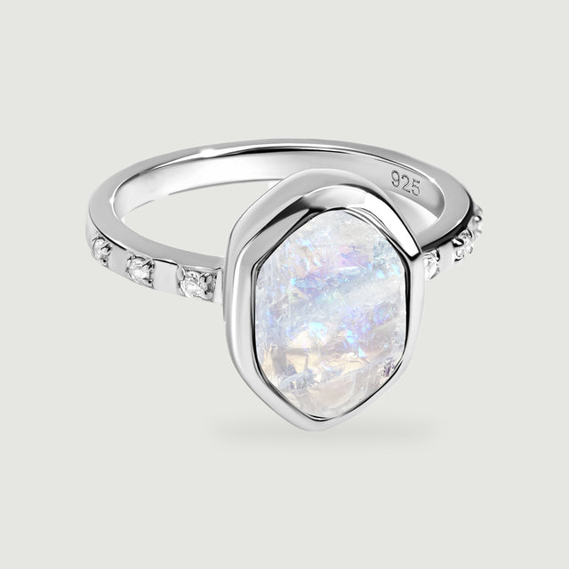 A silver ring shows a raw iridescent moonstone, a polished bezel, and clear stones along the band.