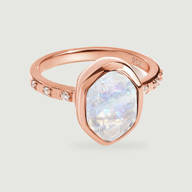 A rose gold ring surrounds a rough white moonstone with a smooth bezel and tiny clear side stones.