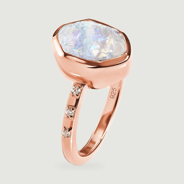 A rose gold ring viewed from the side displays the uneven moonstone face above the polished setting.