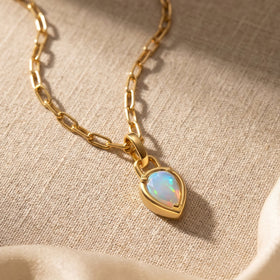 The yellow gold opal necklace rests diagonally on textured beige fabric in warm light.