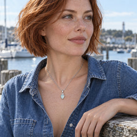 A red-haired woman in a denim shirt wears the silver-tone opal necklace beside a harbor railing.