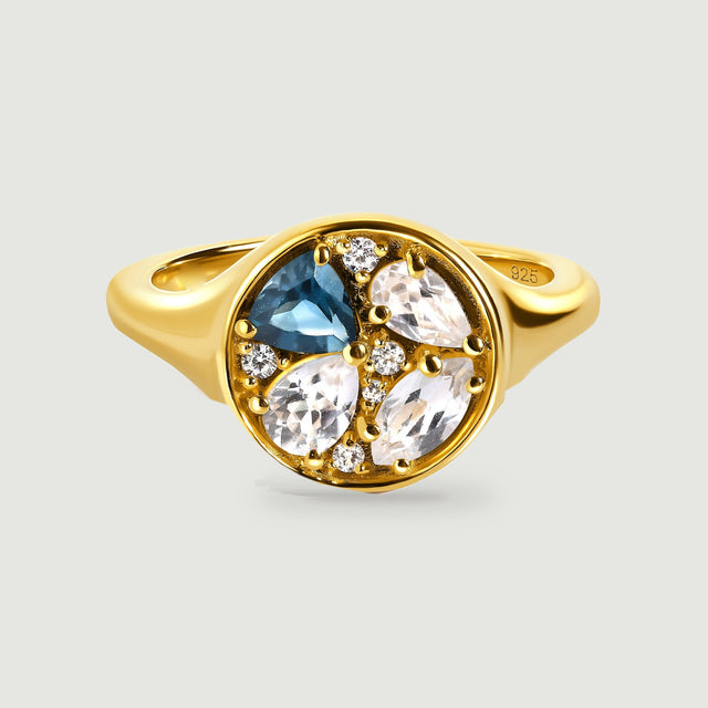 A yellow gold ring displays a round face with one blue stone and three clear pear-shaped stones.