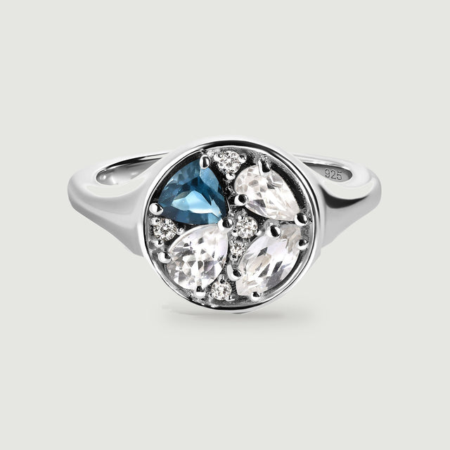 A sterling silver ring shows a blue stone and clear faceted stones within a polished circular face.