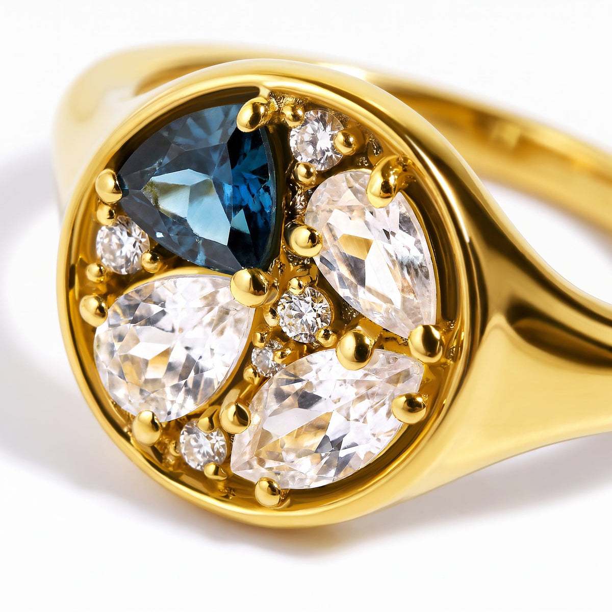 A close view shows the blue gemstone, clear stones, and rounded gold prongs.