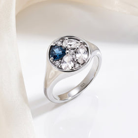 A silver ring rests beside ivory fabric on a clean pale tabletop.