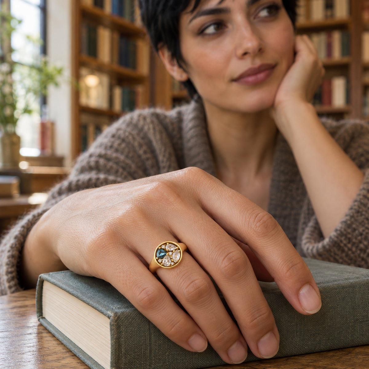 A woman wears the yellow gold ring on her hand resting on a clothbound book.