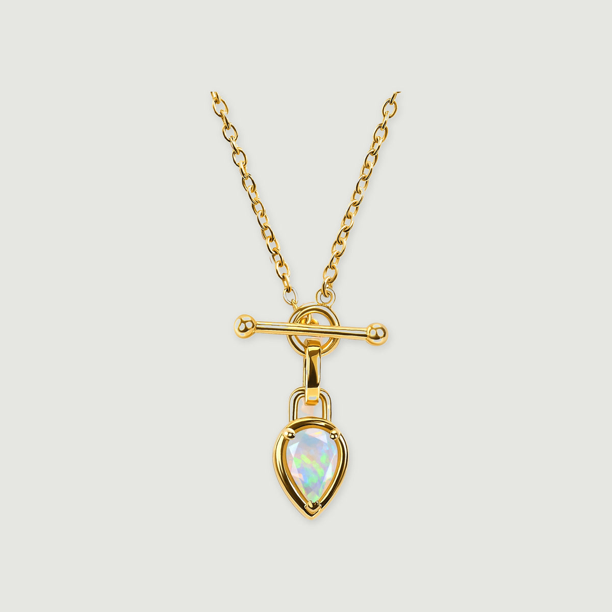 A yellow gold necklace with oval chain links, a horizontal bar, and a pear-shaped opal pendant rests on a light gray background.
