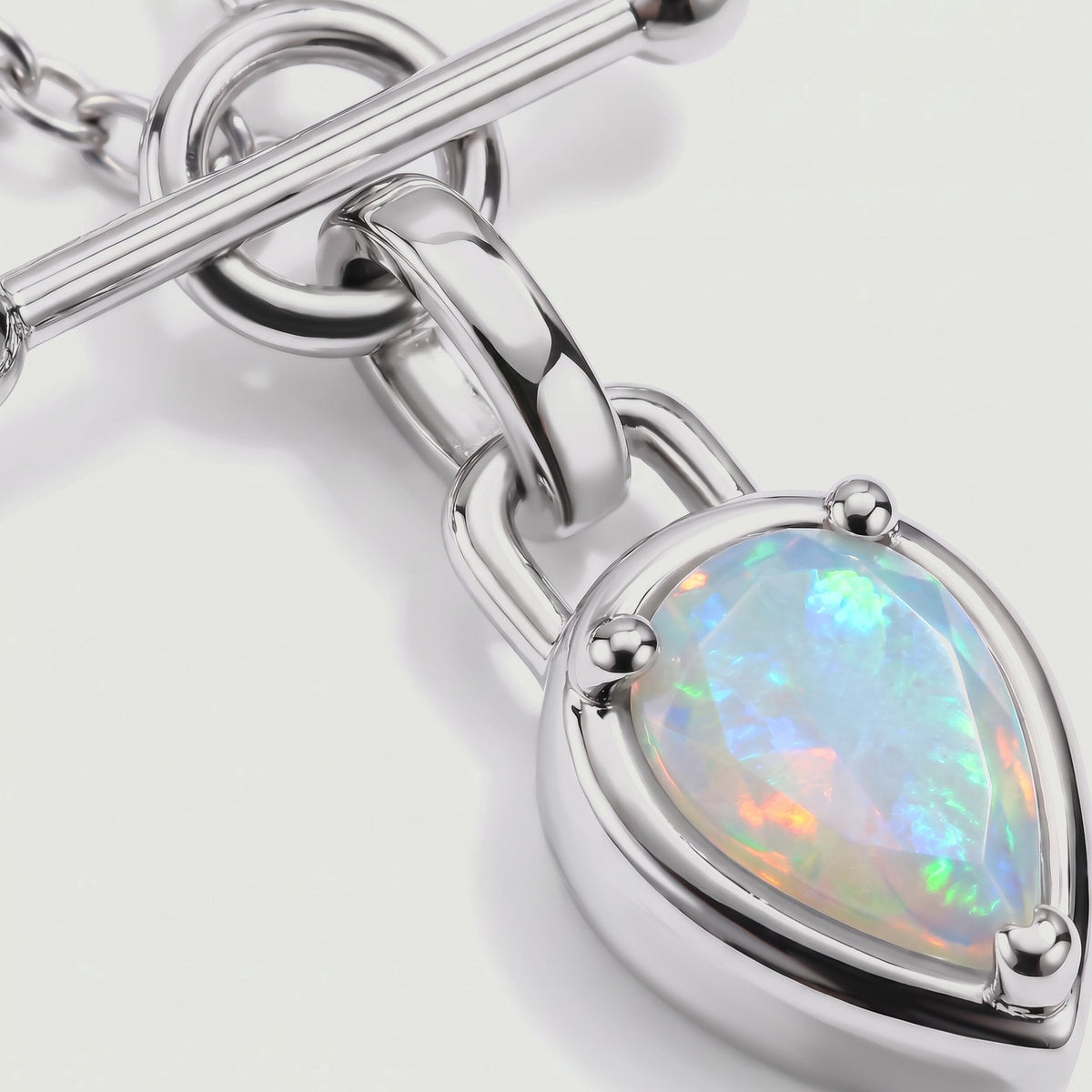 The polished silver-colored setting and raised prongs frame a faceted opal with green, blue, and orange reflections.