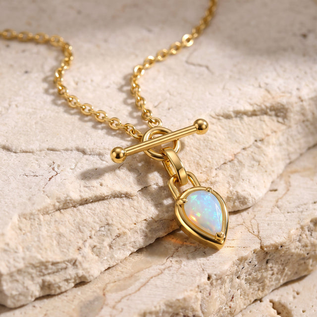 The yellow gold chain and opal pendant lie diagonally across a pale textured stone surface.
