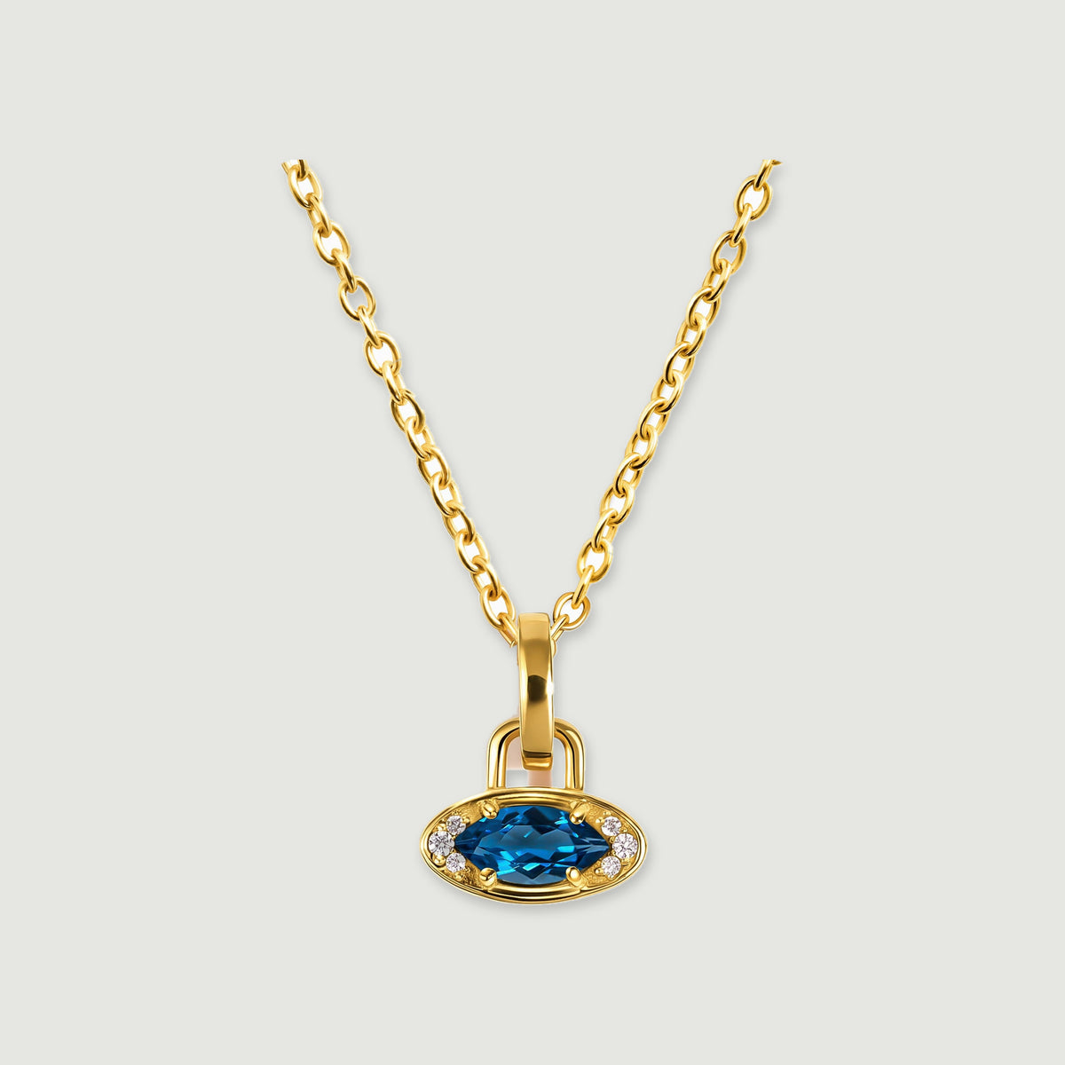 A yellow gold plated chain holds a horizontal blue topaz charm against a light gray background.