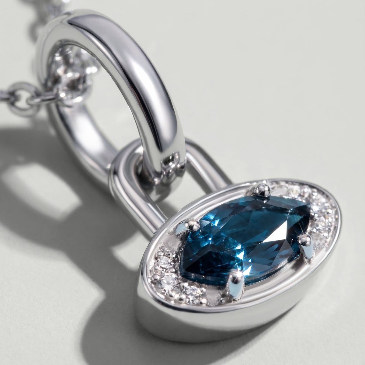 A close view shows the blue topaz facets, four prongs and clear accent stones in a white rhodium plated charm.