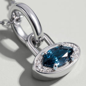 A close view shows the blue topaz facets, four prongs and clear accent stones in a white rhodium plated charm.