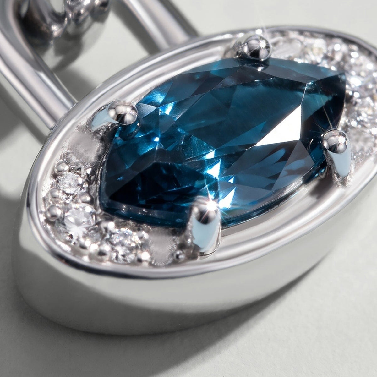 An angled close view reveals the raised blue topaz, curved rim and polished side wall of the white rhodium plated charm.