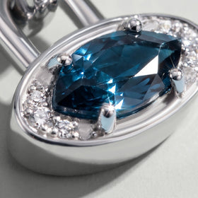 An angled close view reveals the raised blue topaz, curved rim and polished side wall of the white rhodium plated charm.
