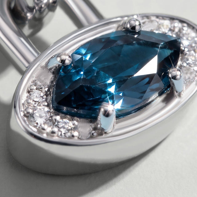 An angled close view reveals the raised blue topaz, curved rim and polished side wall of the white rhodium plated charm.