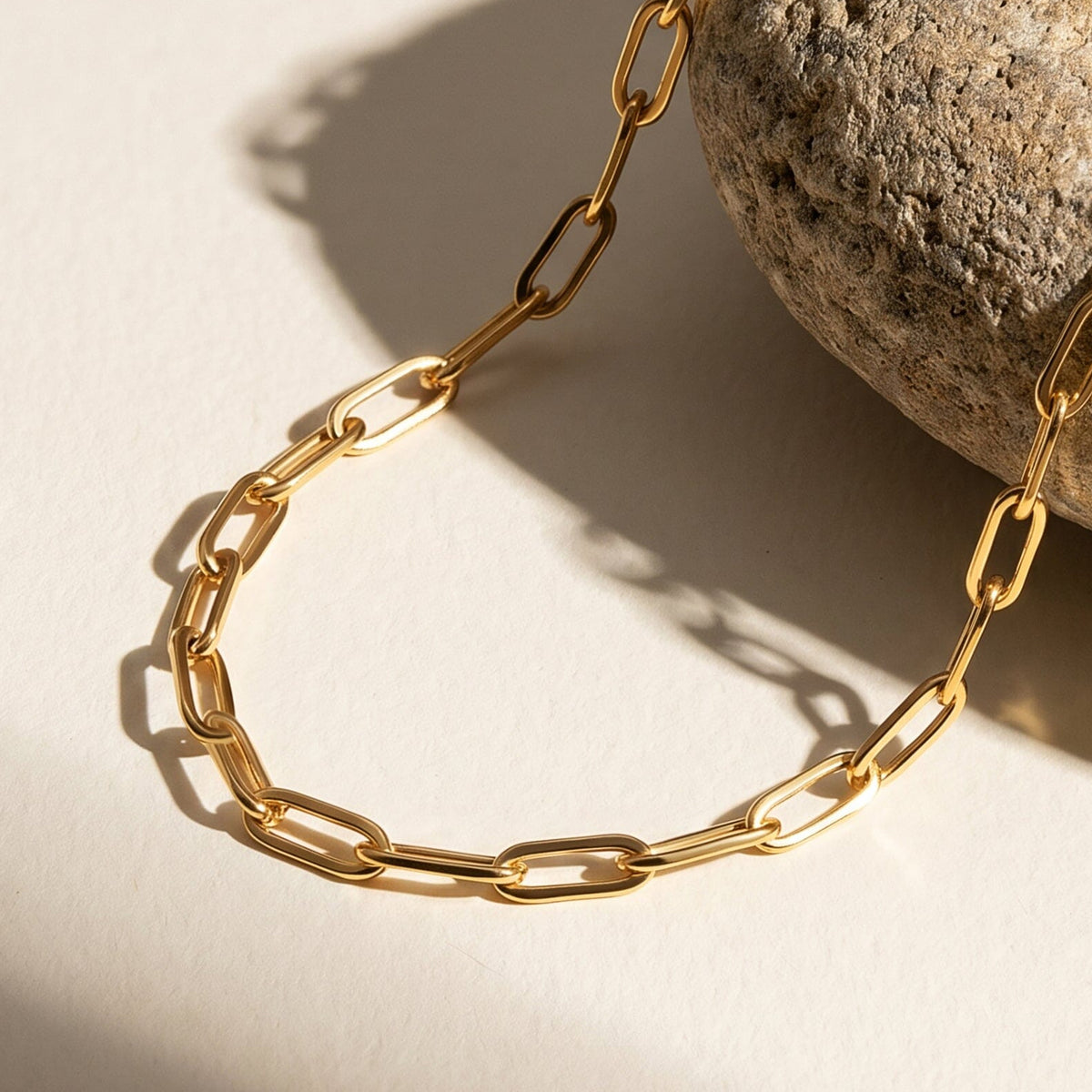 Polished yellow gold plated links curve across a pale tabletop beside the edge of a rounded stone.