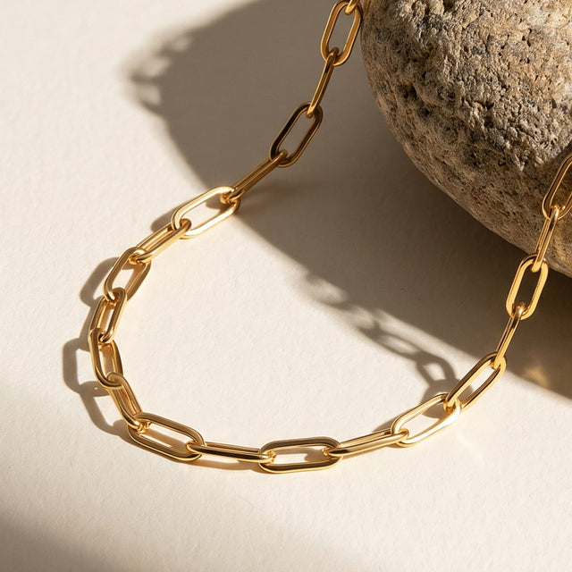 Polished yellow gold plated links curve across a pale tabletop beside the edge of a rounded stone.