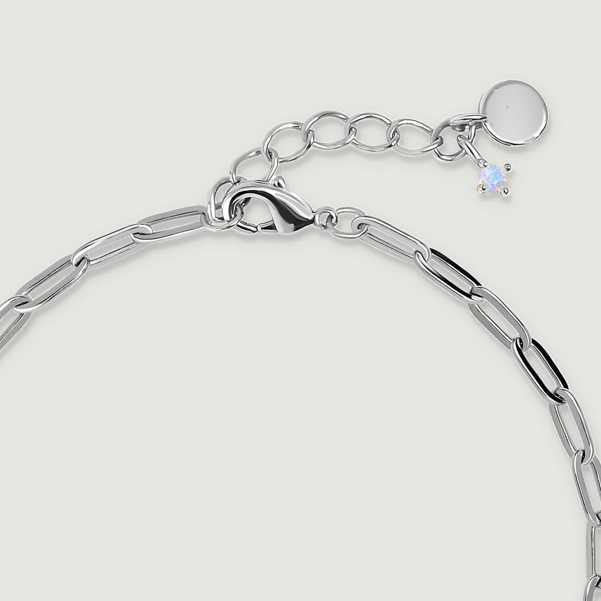 A white rhodium plated lobster clasp sits beside round extension links, a plain round tag, and a small pale charm.