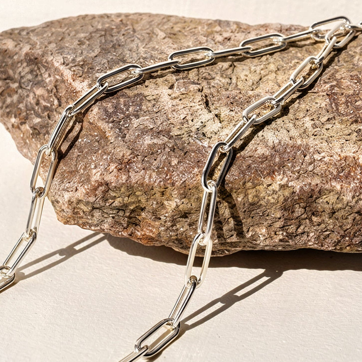Polished white rhodium plated links cross a rough stone and cast slender shadows onto a pale tabletop.
