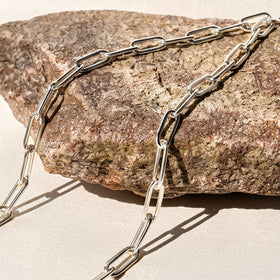 Polished white rhodium plated links cross a rough stone and cast slender shadows onto a pale tabletop.